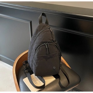 Détail du sac bandoulière en nylon noir montrant le tissu texturé et la poche zippée avant