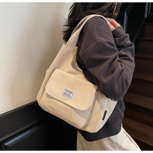 Detail of minimalist beige canvas tote bag with front pocket and branded woven labels