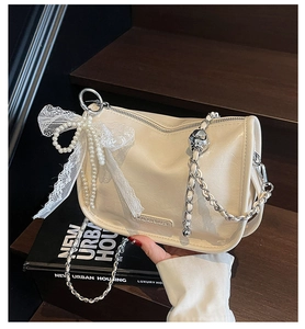 Close-up of cream leather shoulder bag with silver chain and pearl bow charm detail