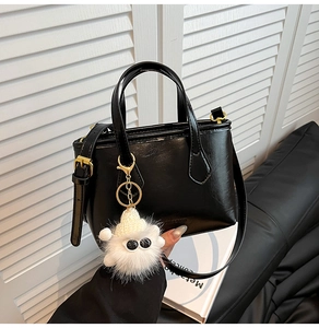 Detail of black glossy patent bucket bag with white plush monster charm and gold hardware