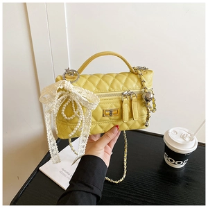 Detailed shot of yellow quilted handbag with lace bow and pearl charm on wooden surface