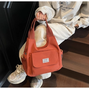 Detail view of orange canvas shoulder bag with front flap pocket and woven side pockets