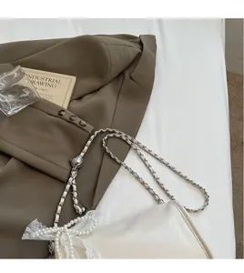 Detail of soft cream leather bag with pearl bow, lace accents and metal chain strap
