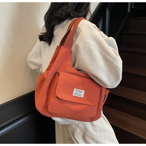 Detail view of brick red canvas shoulder bag with a large front pocket and white label tag