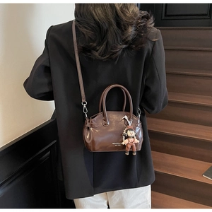 Dettaglio borsa in pelle cerata marrone scuro con ciondolo a bambola e perla elegante