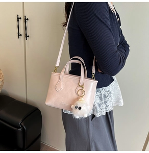 Detail of light pink crossbody bucket bag featuring a white plush charm and gold hardware