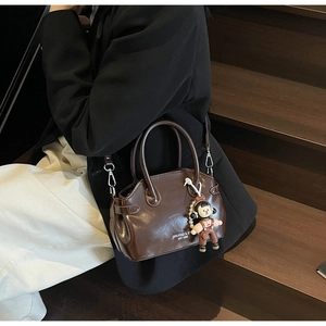 Dettaglio borsa in pelle cerata marrone scuro con ciondoli su scale di legno vintage