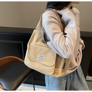 Detail of light khaki canvas shoulder bag featuring a large front flap pocket and logo tag