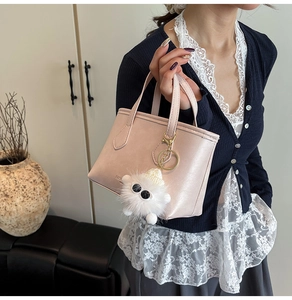 Detail of light pink bucket bag with pearl finish and a white plush monster charm