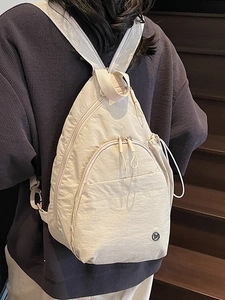 Sac de poitrine minimaliste en nylon blanc cassé avec compartiments zippés porté par un mannequin