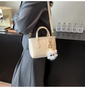 Detail of a cream bucket bag with plush charm and 'Fashion & Bags' embossed text