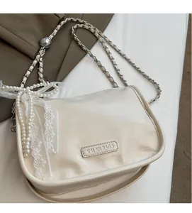 Detail of cream soft faux leather bag featuring a decorative pearl bow charm and chain strap
