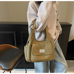 Detailed view of an olive green canvas shoulder bag with a magnetic pocket on a model