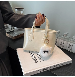 Detail of cream white tote bag with faux leather texture and plush monster charm