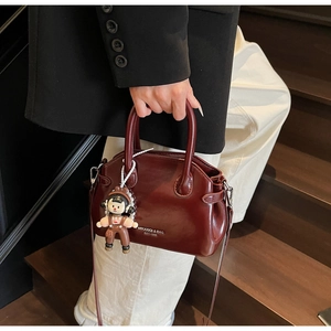 Dettaglio borsa in pelle cerata bordeaux con cinturino di perle e ciondolo cartoon