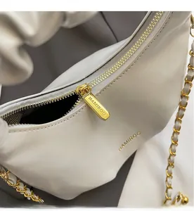 Gros plan sur la fermeture éclair dorée et le cuir de ce sac à main blanc plissé