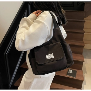Close-up of black canvas shoulder bag featuring a front pocket with a white textile label