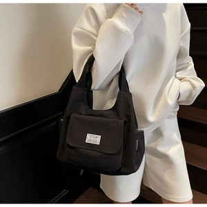Detail of black canvas tote bag with front pocket and durable handles on model