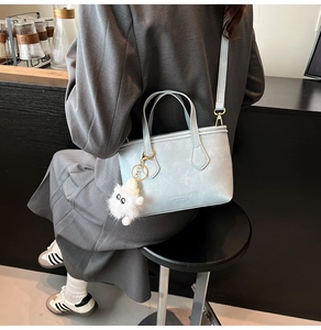 Detail view of light blue leather bucket bag with plush charm and fashion logo