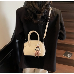 Dettaglio della mini borsa in pelle bianco crema con ciondolo carino su scalini in legno