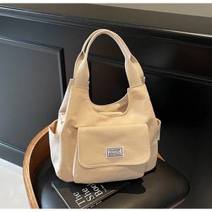 Detail of minimalist beige canvas shoulder bag with front pocket on a leather chair