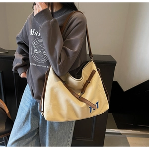 Detail of canvas tote bag with brown leather strap and blue letter embroidery
