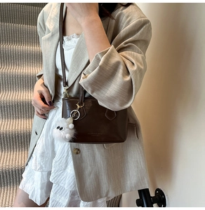 Detail of a dark brown vintage crossbody bag with a white plush charm on a staircase
