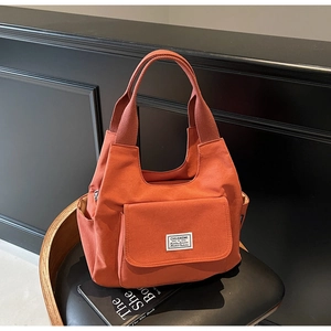 Detail of orange canvas shoulder bag featuring a front pocket with branded woven label