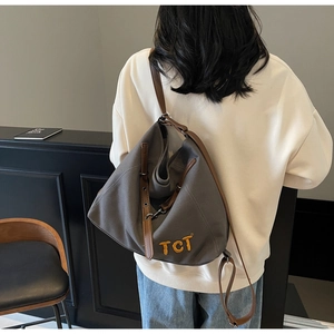 Detail of grey canvas tote bag with yellow TCT embroidery and leather strap on model