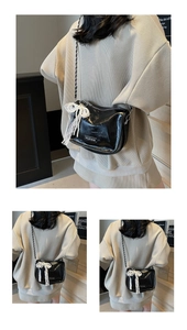 Detail of black patent leather bag with white lace pearl bow and gold chain strap