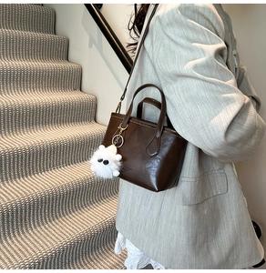 Detailed shot of dark brown matte PU leather handbag with a cute white plush monster charm
