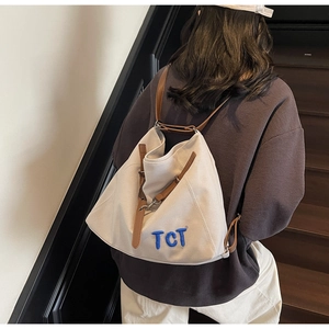 Detail view of cream canvas tote bag featuring brown leather straps and blue TCT embroidery