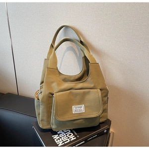 Detail view of the green canvas tote bag featuring a front flap pocket and woven handle
