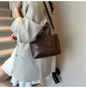 Close-up of small brown bucket bag with gold lettering and adjustable shoulder strap detail