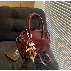 Dettaglio borsa Boston in pelle cerata bordeaux con ciondolo di perle su divano