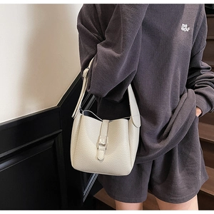 Detail of light beige litchi grain leather bucket bag with silver buckle on a model