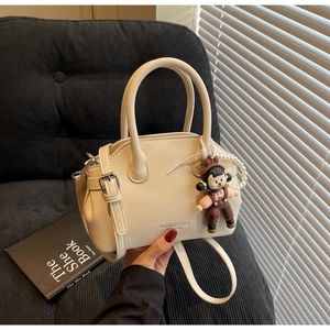 Dettaglio della borsa in pelle bianco crema con tracolla regolabile e ciondolo a bambola