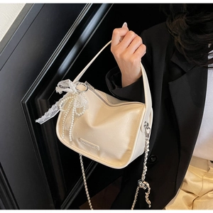 Detail of soft cream leather pillow bag featuring elegant lace and pearl bow charm