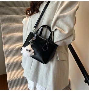Detail of black tote bag with clear texture, shoulder strap and white plush monster charm