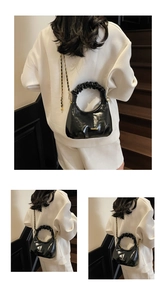 Détail du sac noir brillant avec poignée plissée et bandoulière en chaîne dorée