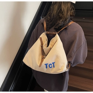Detailed back view of a beige canvas backpack featuring a blue TCT embroidery logo