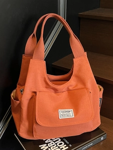 Minimalist orange canvas tote bag with front pocket shown on a stylish wooden step