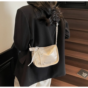 Detail of a creamy beige leather crossbody bag with lace bow and pearl charm on a model