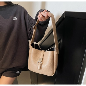 Detail view of beige pebble grain leather bucket bag with metallic square clasp on model