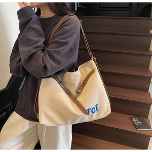 Detailed view of large off-white canvas tote bag with brown leather handles and TCT embroidery