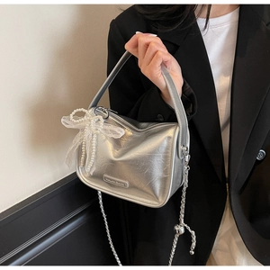 Detail of silver pillow bag featuring lace bow, pearls, and metal brand logo