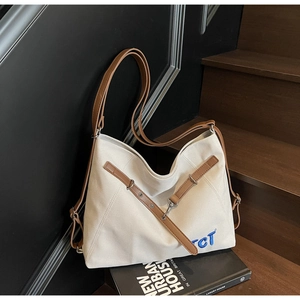 Close-up of beige canvas tote with brown leather handles and blue TCT embroidery detail
