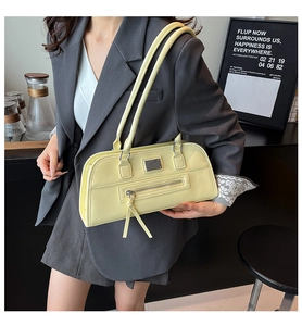Détail du sac sous le bras jaune avec poche zippée et plaque en métal dans un café urbain