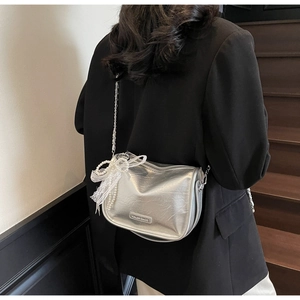 Detail of silver metallic saddle bag with pearl chain and lace bow charm on model