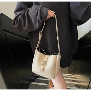 Detail of lychee textured leather bucket bag in cream with elegant metal buckle closure